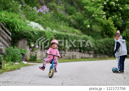 A group of children, including a boy and girl playing with a ball and their young friend riding a bike, enjoying a fun filled day in a natural outdoor setting 122172706