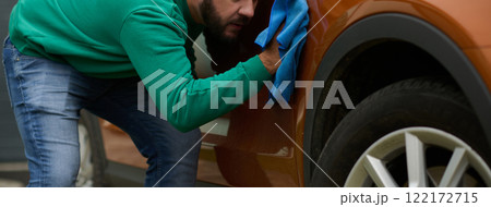 A man meticulously washes and cleans his car in the driveway of his home, showcasing pride in his vehicle and outdoor space. 122172715