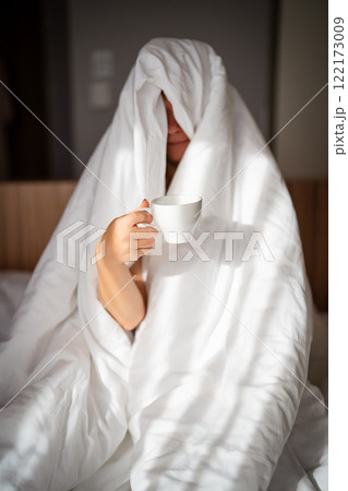 Woman with cup of coffee in the morning under the blanket at home Woman with cup of coffee in the morning under the blanket at home 122173009