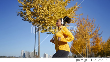 Tired Plus-Size African Woman Running in a City Park on an Autumn Morning with Headphones. Generated image 122173327