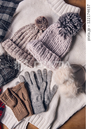 Cozy knit hats, gloves, scarves, and earmuffs displayed on knitted sweater, showcasing winter fashion essentials with soft textures and neutral colors. 122174637