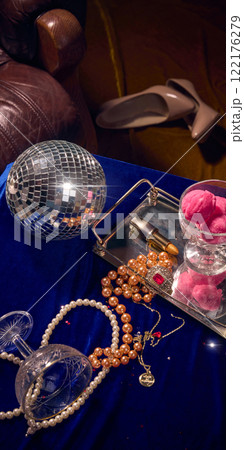 Shimmering disco ball, pink ice cream, pearls, and lipstick on a silver tray atop a deep blue velvet table, evoking a glamorous celebration. 122176279