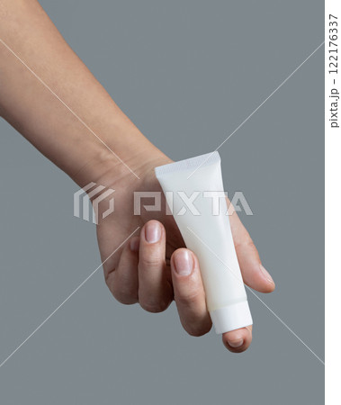 Female hand holding white cream tube against grey close up, cosmetic mockup, copy space Female hand holding white cream tube against grey close up, cosmetic mockup, copy space 122176337