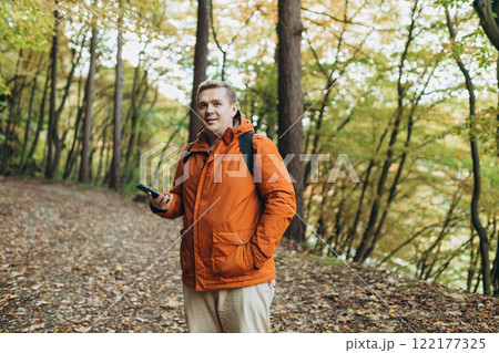 Young Caucasian 30s man backpacker with smartphone catching signal at wooden forest. Road trip, transport, travel, technology and people concept. High quality photo 122177325