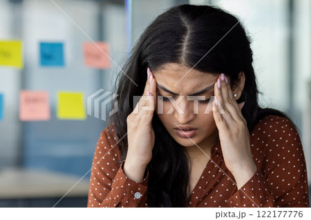 Headache and stress at workplace inside office. Young woman holding hands on head. Businesswoman overworked suffering at workplace inside office close up. 122177776