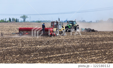 Farmers using tractors to plant seeds in a large field on a sunny day Farmers using tractors to plant seeds in a large field on a sunny day 122180112