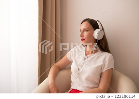 Woman enjoying music while sitting in a cozy chair by the window Woman enjoying music while sitting in a cozy chair by the window 122180114