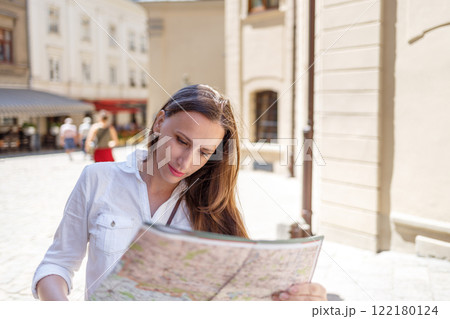 Young woman exploring a cobblestone street while studying a map on a sunny day in a historic city Young woman exploring a cobblestone street while studying a map on a sunny day in a historic city 122180124