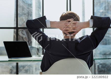 worker sitting in office with hands behind his head 122180922
