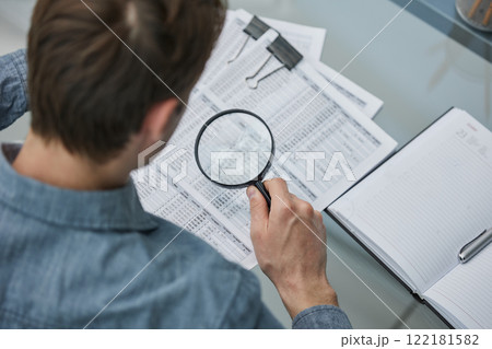 Businessman looking through a magnifying glass to documents note in the office. Businessman looking through a magnifying glass to documents note in the office. 122181582