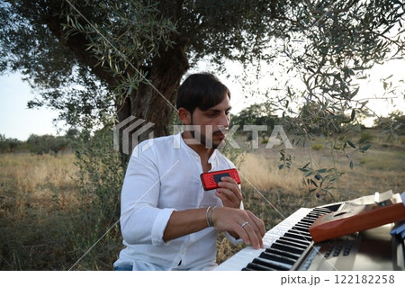 Boy Plays Music With Harmonica And Keyboard Among The Olive Trees Of Calabria 122182258