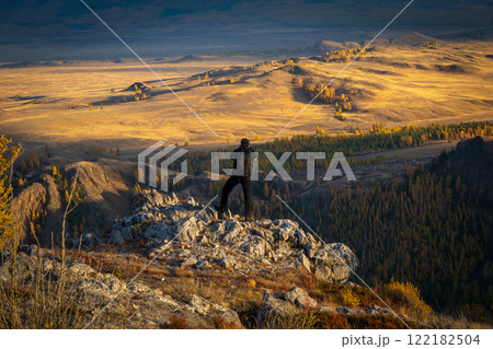 Traveler standing on rocky hill overlooking vast golden autumn landscape 122182504