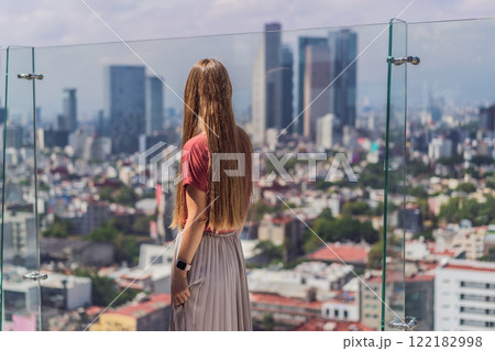 Female tourist or businesswoman standing on a skyscraper rooftop with a panoramic view of Mexico City. Travel or international business in Mexico concept 122182998