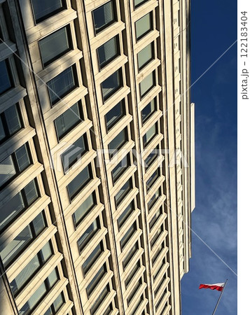 abstract fragment of a monumental moderate Art Nouveau-style office building from the mid-20th century against the blue sky and clouds, the former House of the Party in Warsaw with flag of Poland 122183404