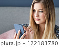 Woman with long blonde hair and blue eyes looking at her smartphone, online shopping, work from home lifestyle idea 122183780