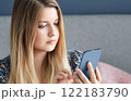 Woman with long blonde hair and blue eyes looking at her smartphone, online shopping, work from home lifestyle idea 122183790