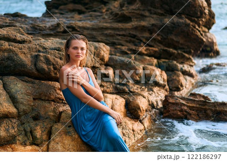 Model woman poses in wet dress by ocean rocks on exotic island. Scenic backdrop with stormy sea, vibrant landscape. Elegance in natural setting. Ideal for travel, fashion, tropical themes. Model woman poses in wet dress by ocean rocks on exotic island. Scenic backdrop with stormy sea, vibrant landscape. Elegance in natural setting. Ideal for travel, fashion, tropical themes. 122186297