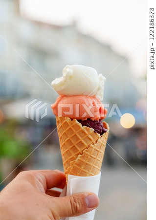 Delicious hand holding a colorful ice cream cone with three tasty scoops of ice cream in summer sun 122186378