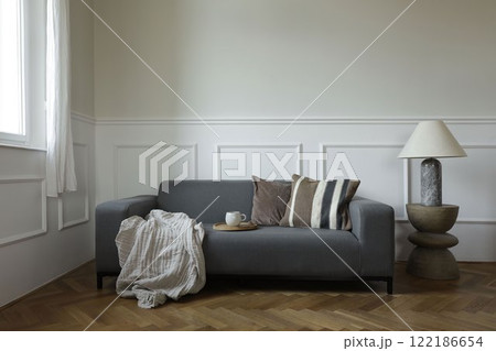 Cozy Scandinavian living room. Grey couch with brown natural cushions near window. Modern boho wooden coffee table, marble lamp. Oak parquet flooring. Cup of tea, coffee. Elegant neutral home decor. Cozy Scandinavian living room. Grey couch with brown natural cushions near window. Modern boho wooden coffee table, marble lamp. Oak parquet flooring. Cup of tea, coffee. Elegant neutral home decor. 122186654