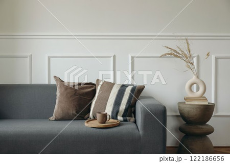 Grey sofa with brown pillows. Empty beige wall mockup. Cup of tea, coffee on wooden tray. Boho living room interior. Modern vase with dry flowers grass. Minimalist home decor. Scandinavian design Grey sofa with brown pillows. Empty beige wall mockup. Cup of tea, coffee on wooden tray. Boho living room interior. Modern vase with dry flowers grass. Minimalist home decor. Scandinavian design 122186656