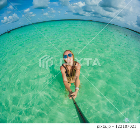 Woman standing in the crystal-clear waters of Lake Bacalar, Mexico, enjoying the serene beauty of the landscape. Tranquil moment in nature, outdoor escape, and relaxation concept Woman standing in the crystal-clear waters of Lake Bacalar, Mexico, enjoying the serene beauty of the landscape. Tranquil moment in nature, outdoor escape, and relaxation concept 122187023