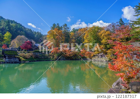 青空バックに見るちょうど見ごろの紅葉に囲まれた合掌造りの里の情景 122187317