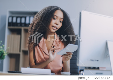 Young caucasian business woman counting funds, planning budget, paying bills online using calculator. Freelancer boss CEO doing paperwork with finances. Young caucasian business woman counting funds, planning budget, paying bills online using calculator. Freelancer boss CEO doing paperwork with finances. 122188752