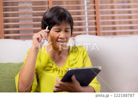 Senior asian woman sitting on sofa using digital tablet with relax in living room at home. 122188787