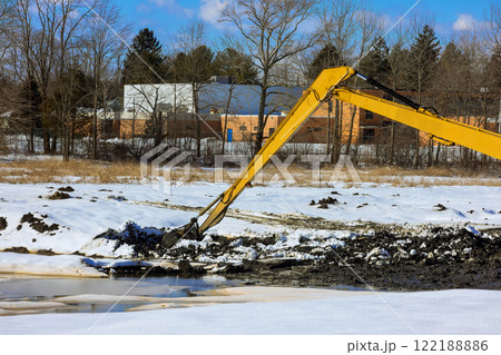 Heavy excavator machinery removes earth, snow at under construction site during winter. 122188886