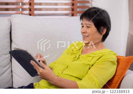 Senior asian woman sitting on sofa using digital tablet with relax in living room at home. 122188915