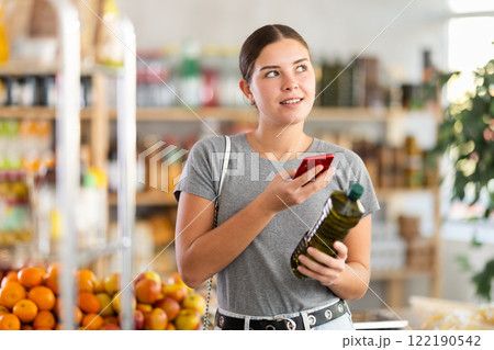 In shop youth girl scan QR code and take reading olive oil package bottle using phone camera In shop youth girl scan QR code and take reading olive oil package bottle using phone camera 122190542