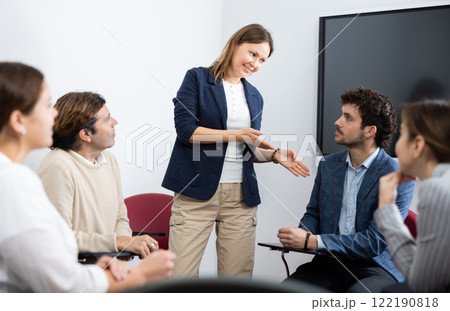 Positive successful female teacher listening to answers from students of different ages while they sitting in circle at foreign language lesson Positive successful female teacher listening to answers from students of different ages while they sitting in circle at foreign language lesson 122190818