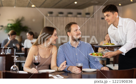 Waiter brings order to young man and woman couple Waiter brings order to young man and woman couple 122190836
