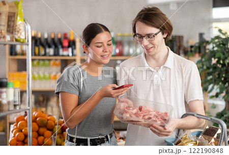 In shop youth spouses scan QR code and take reading raw pork tenderloin package using phone camera In shop youth spouses scan QR code and take reading raw pork tenderloin package using phone camera 122190848