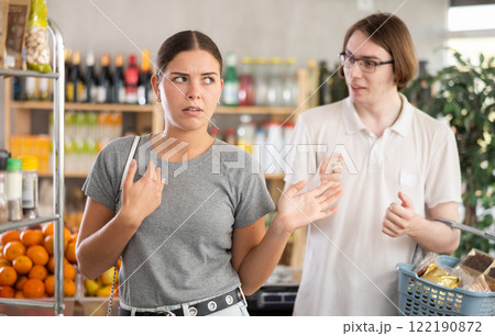 In shop guy stands behind wife, hurling abuse and indignation at her. 122190872