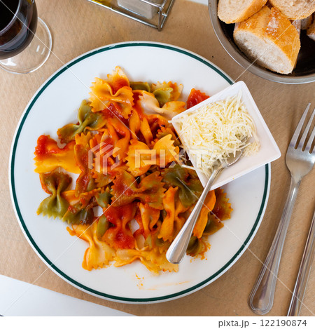 Bow form pasta with tomato sauce is served with bowl of grated cheese. 122190874
