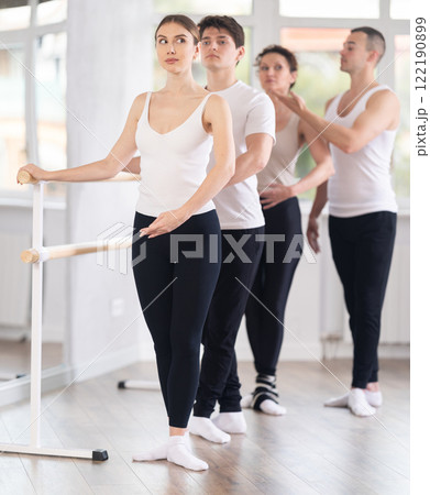Young man trainer corrects dancers at barre 122190899