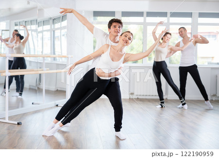 Acrobatic couple perform ballet pose with support during group training class in ballet hall 122190959
