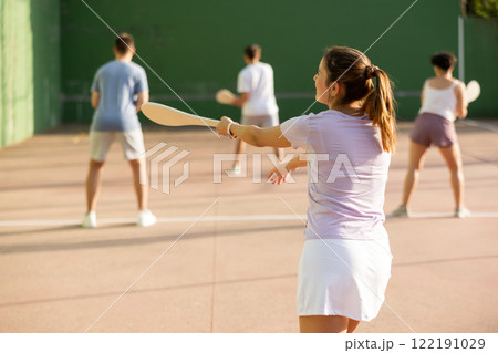 Active womans with enthusiasm playing paleta fronton group on outdoor court 122191029