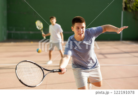 Young frontenis player swinging racquet to hit ball on outdoor court Young frontenis player swinging racquet to hit ball on outdoor court 122191078