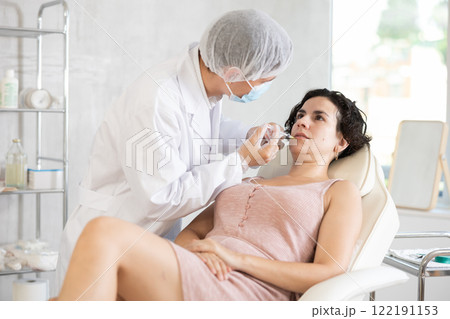 Qualified cosmetologist giving beauty injections for face skin rejuvenating and tightening for female client in aesthetic medicine office 122191153
