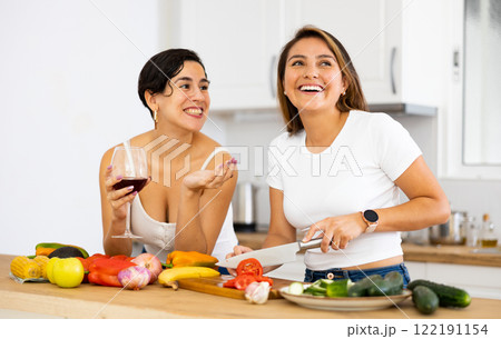 Two cheerful female roommates drinking wine and preparing dinner at home 122191154