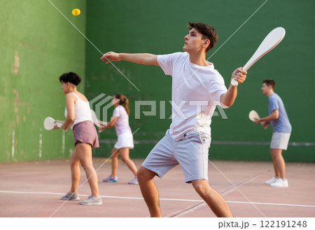 Guy playing pelota at open-air fronton, swinging wooden bat to return ball Guy playing pelota at open-air fronton, swinging wooden bat to return ball 122191248