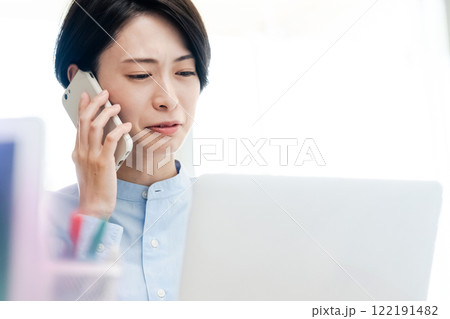 パソコンの画面を見ながら電話をする若い女性 122191482