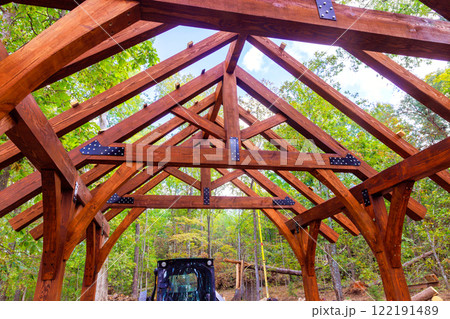 Wooden framework framework gazebo under clear sky, surrounded by trees tractor ready for construction work. 122191489