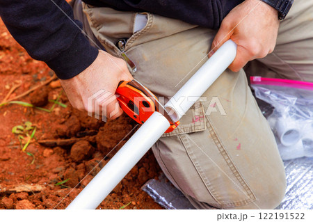 Plumber is using cutting tool to accurately shorten PVC pipe in dirt area during plumbing water line installation 122191522