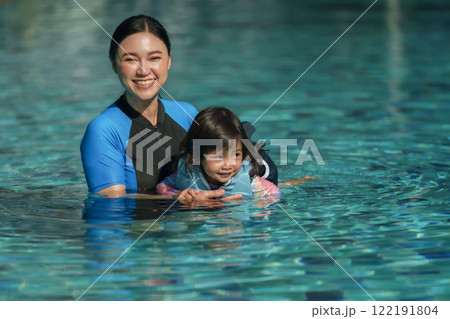 mother teaching toddler baby girl swimming in pool and wearing life jacket 122191804