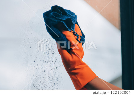Young female worker cleaning window glass with cloth in spacious villa 122192004