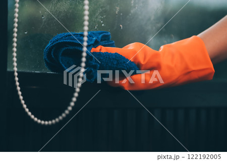 Young female worker cleaning window glass with cloth in spacious villa 122192005