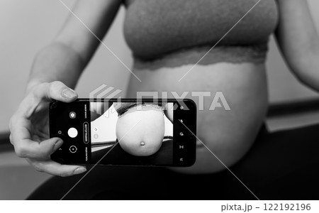 Pregnant woman taking a photo of her belly Pregnant woman taking a photo of her belly 122192196
